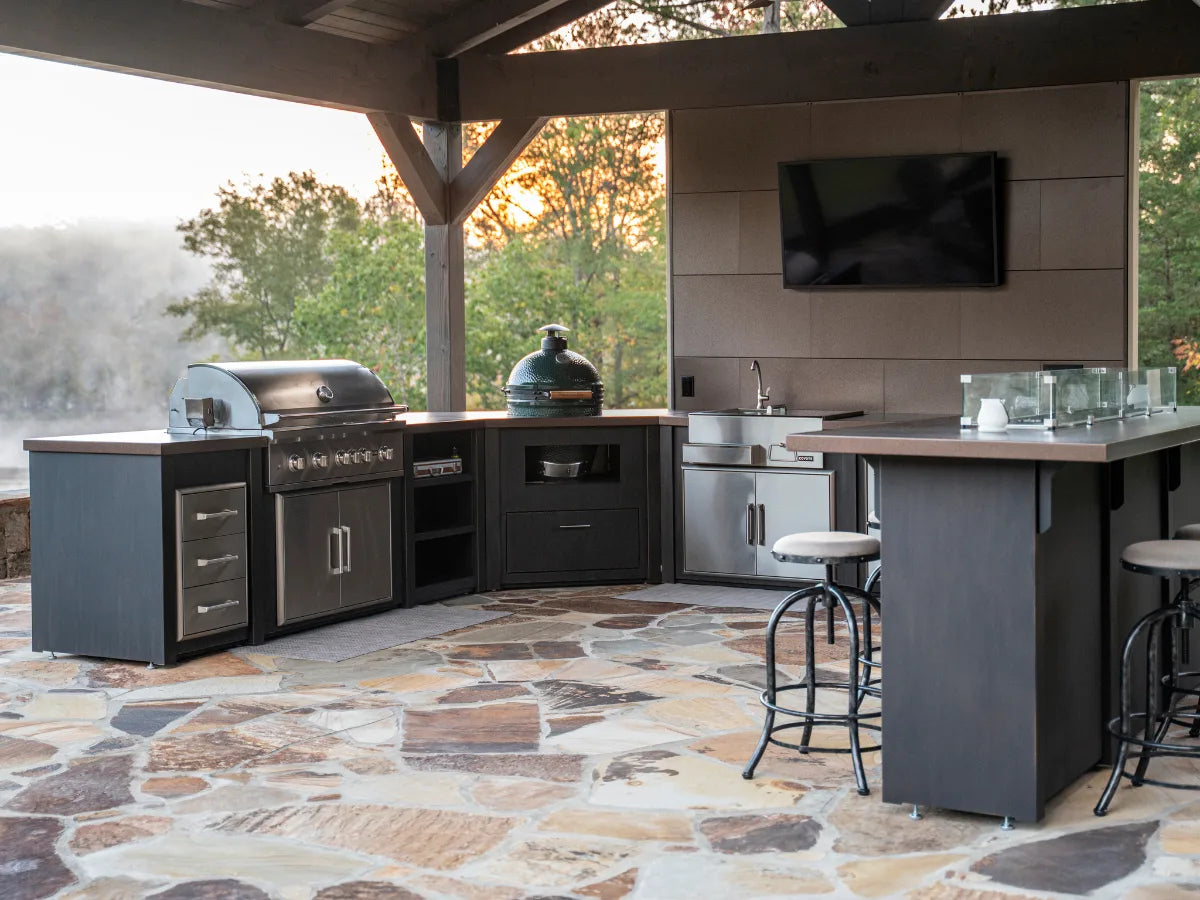 Outdoor kitchen with grill, sink, and TV in a wooded area