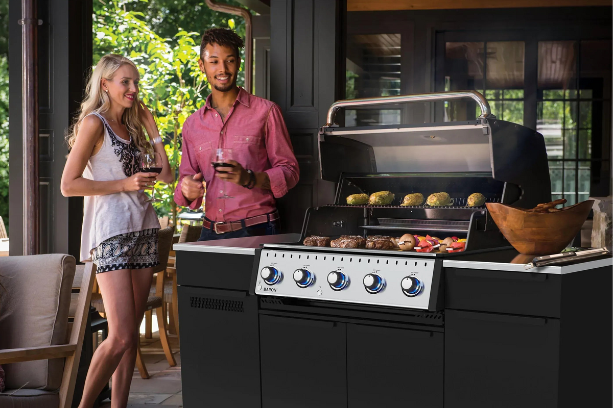 Two people standing next to a barbecue grill with food on it outdoors.